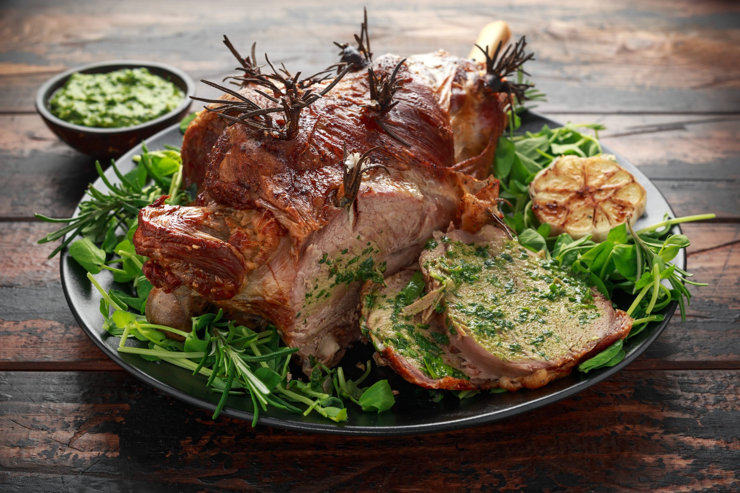 Roast Lamb leg with mint sauce, rosemary and garlic. on black plate, wooden table