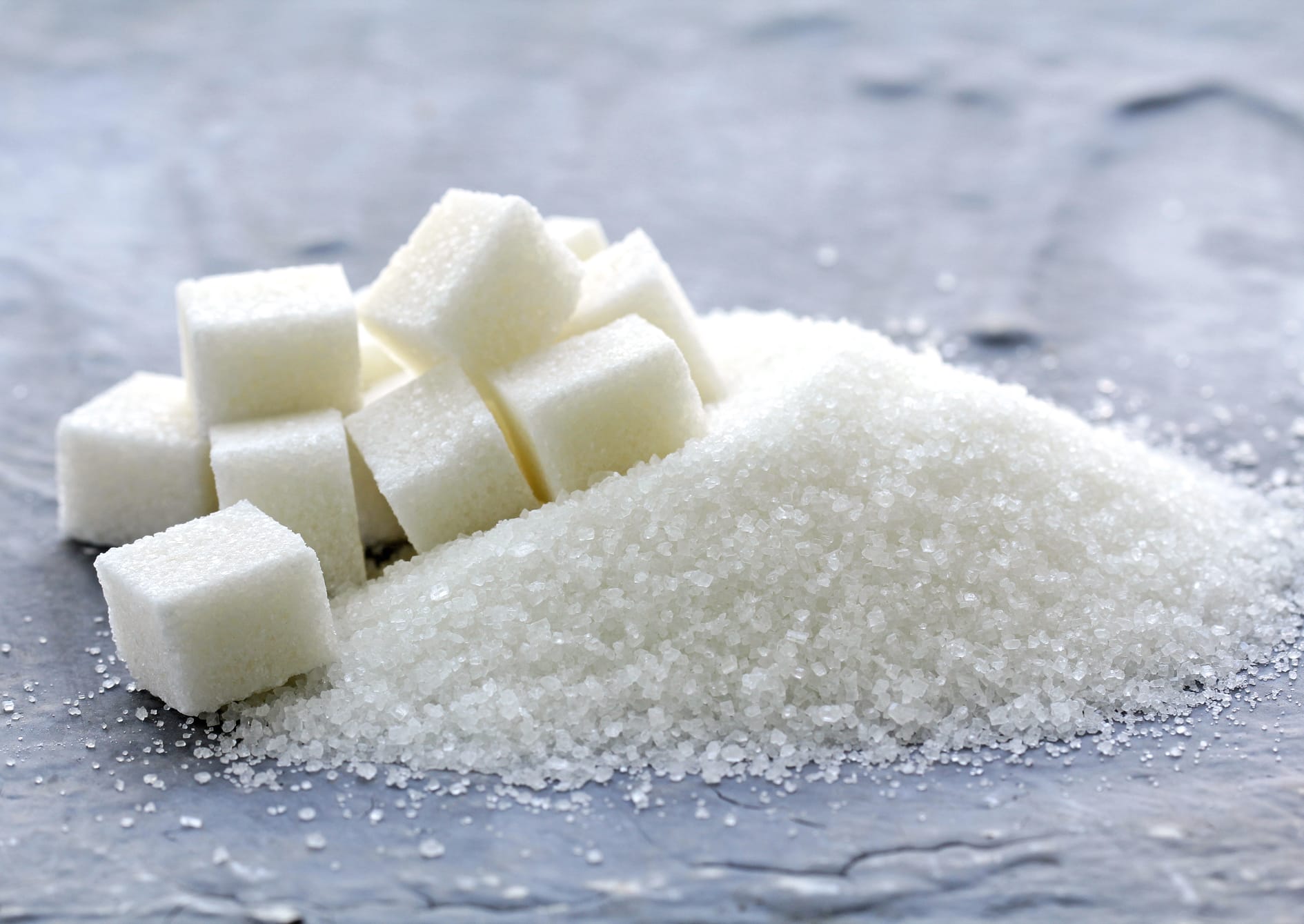 white granulated sugar and refined sugar on a gray background